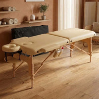 Table de massage pliante en bois Colette Sable de Lune en cabinet, housse de transport noire posée contre le mur